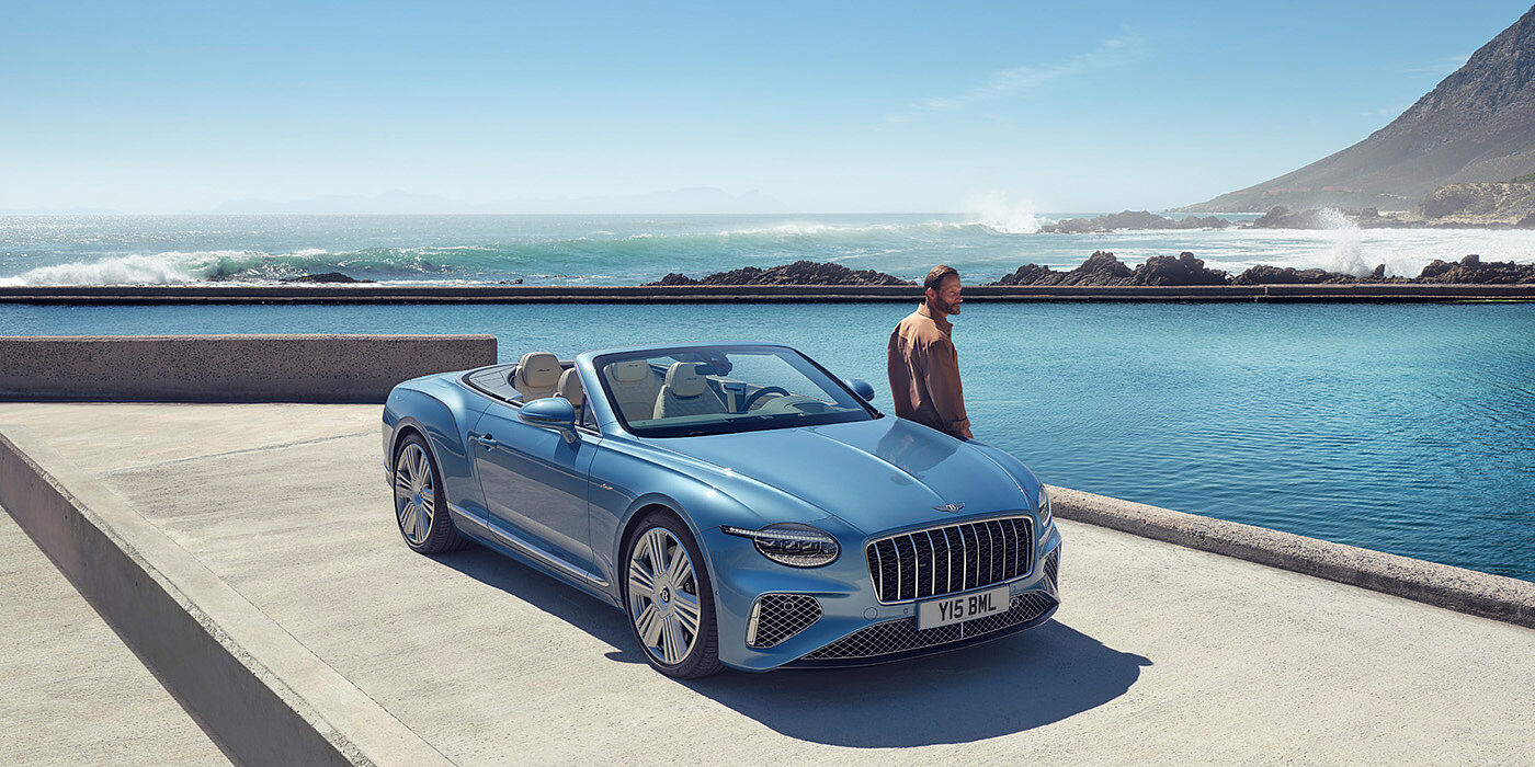 Bentley Marbella New Bentley Continental GTC Azure convertible front view in Light Windsor blue paint with 22 inch ten spoke wheels parked by the sea in the sunshine