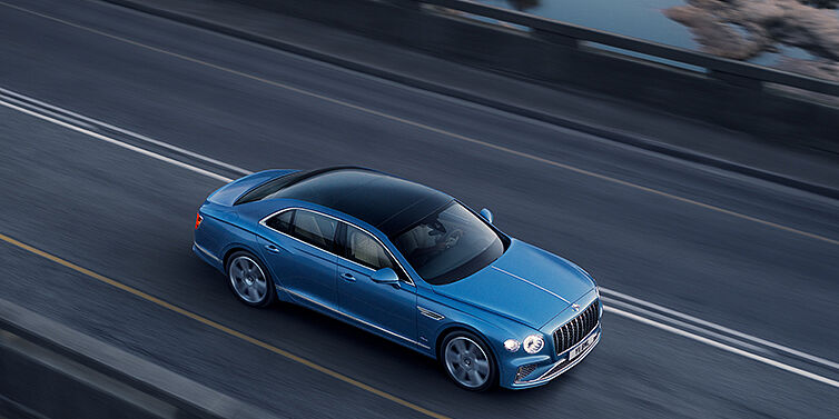 Bentley Marbella New Bentley Flying Spur Azure sedan in Light windsor blue paint by Mulliner, with 22 inch Azure wheels seen from overhead driving dynamically on a country road
