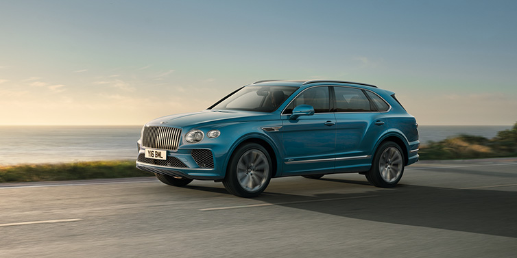 Bentley Marbella Bentley Bentayga Azure SUV in Topaz blue paint driving dynamically by the ocean with 22 inch 10 spoke directional wheels