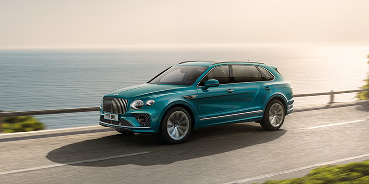 Bentley Marbella Bentley Bentayga Extended Wheelbase Azure SUV in Topaz blue paint driving dynamically by the ocean