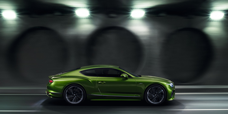 Bentley Marbella Bentley Continental GT Speed coupe profile in Tourmaline Green driving dynamically past a concrete wall at night