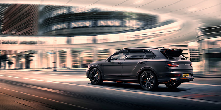 Bentley Marbella Bentley Bentayga S Black Edition SUV rear three quarter in Anthracite Satin paint driving dynamically through a city at night