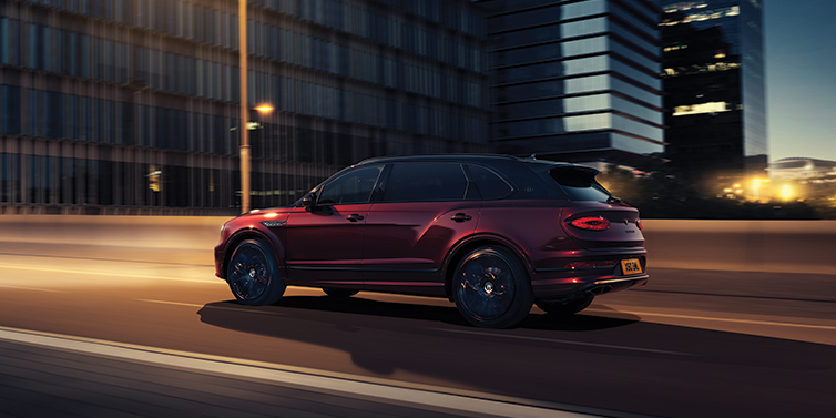 Bentley Marbella Bentley Bentayga Extended Wheelbase Mulliner SUV in Cricket Ball red paint driving dynamically in city at night