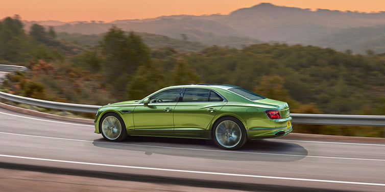 Bentley Marbella Bentley Flying Spur Speed sedan side profile in Tourmaline Green paint driving dynamically on a mountain road at sunset